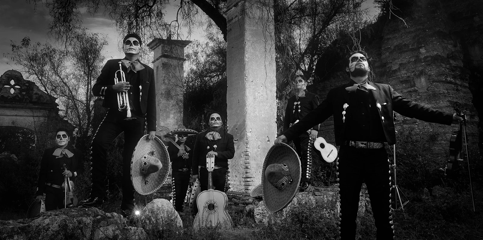 grupo de hombres con ropa de mariachi sujetando instrumentos y maquillados de calaveras